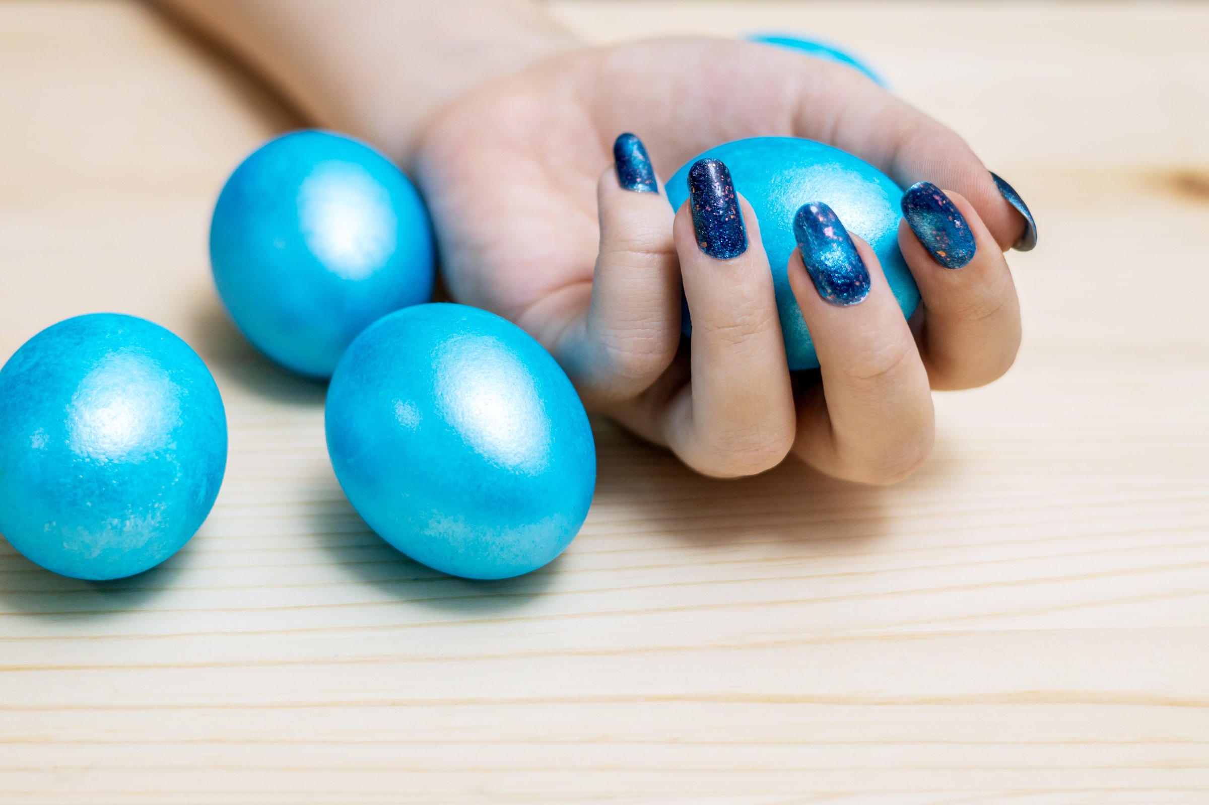 Hand of a young woman with beautiful magnetic nail polish holding blue colored Easter eggs. Horizontal manicure photo.