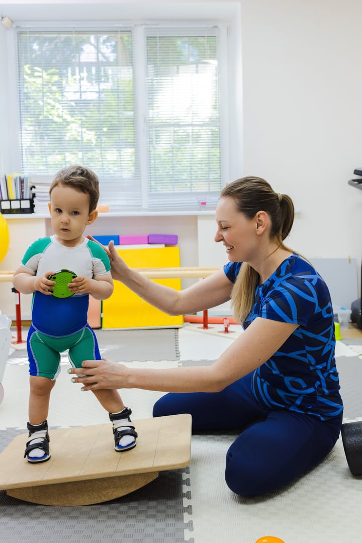 Physiotherapist assisting young child with coordination exercise in rehabilitation center. Neurological rehabilitation for child with therapeutic physiotherapy