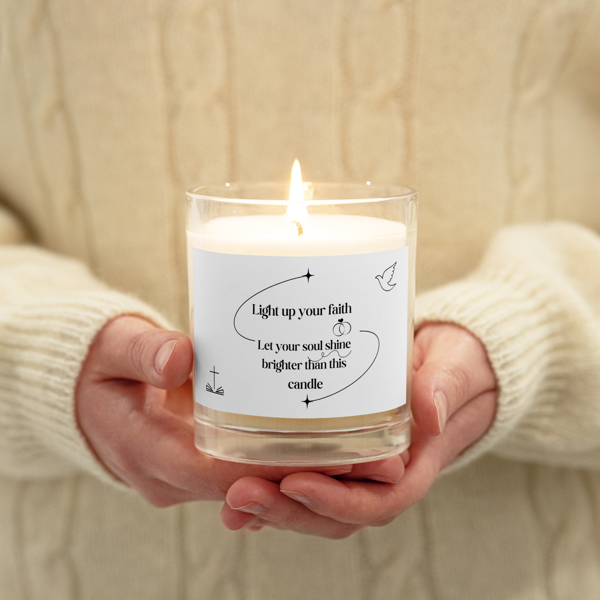 Person holding a lit candle in a glass jar with an inspirational message on the label.