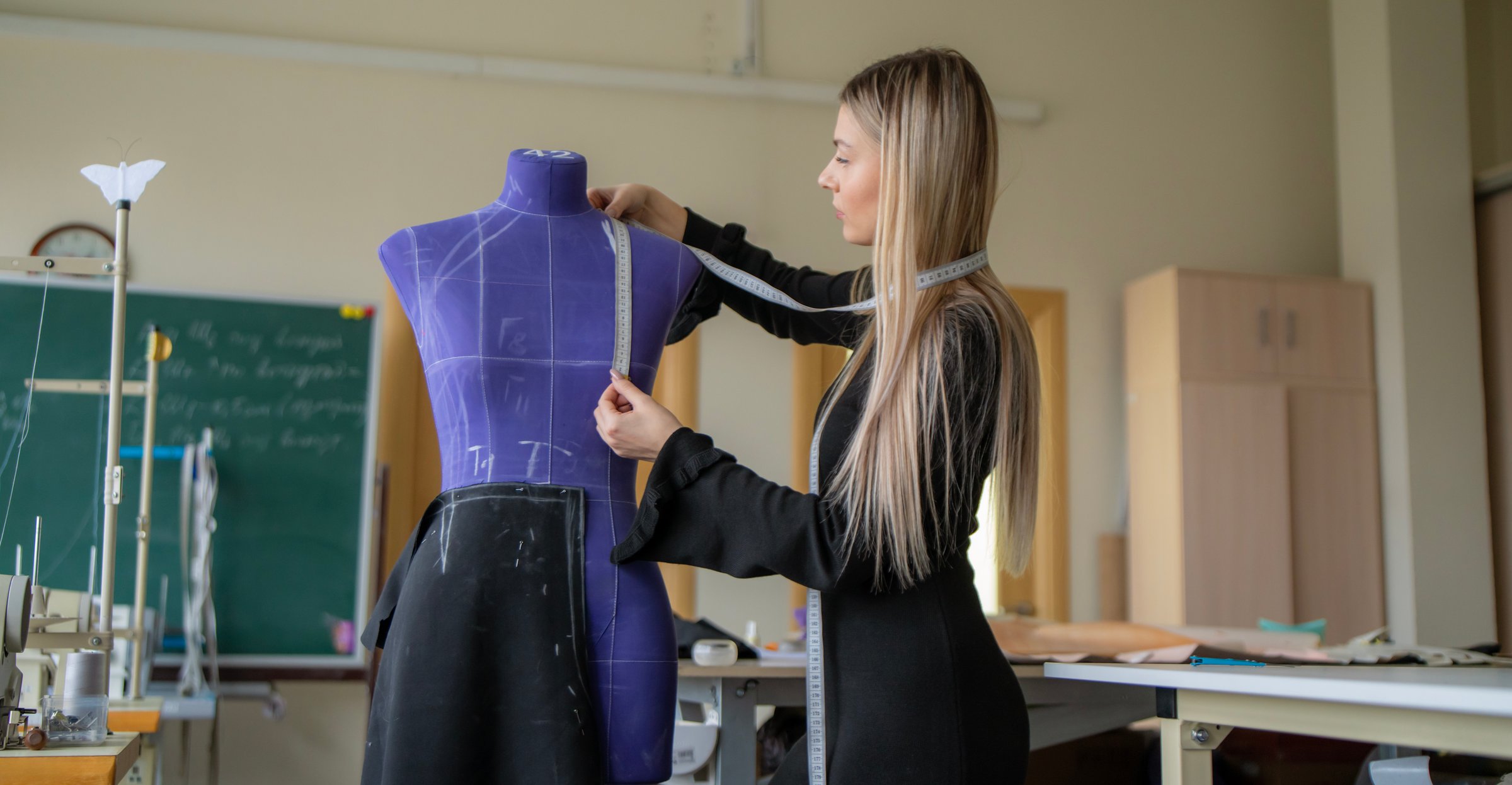 Student carefully measures fabric around the waist of a mannequin and try on a pattern in a sewing workshop during a design project
