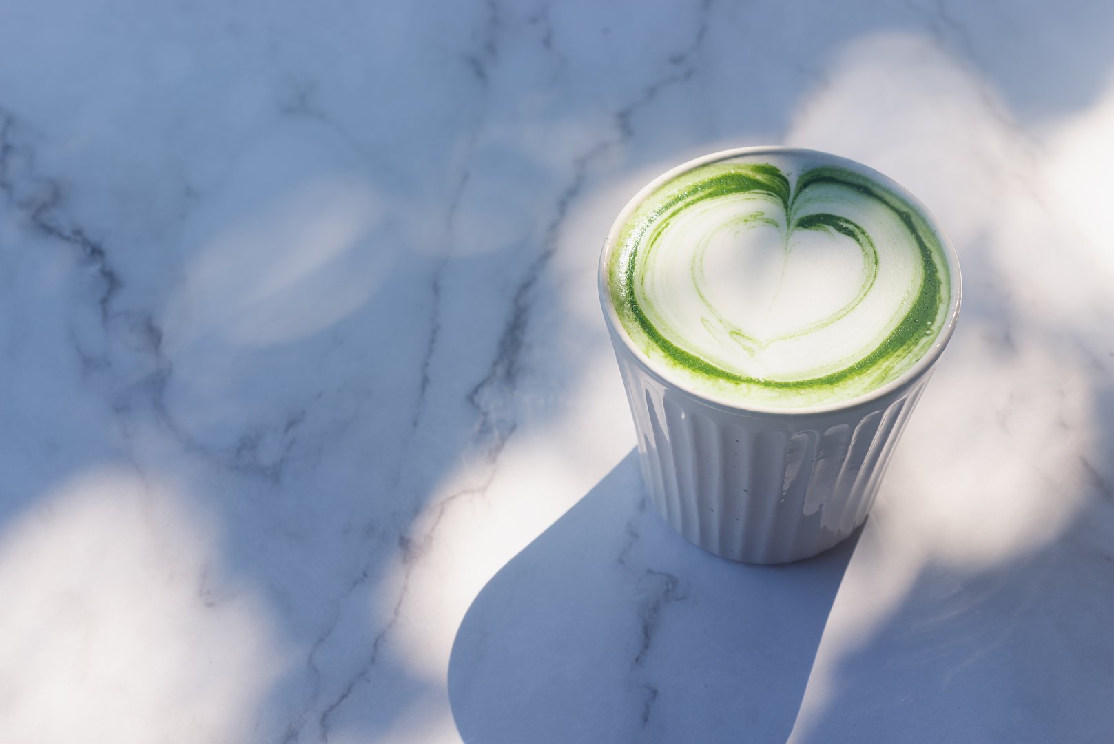 hot matcha latte in white ceramic cup on marble table background in the morning sunlight.