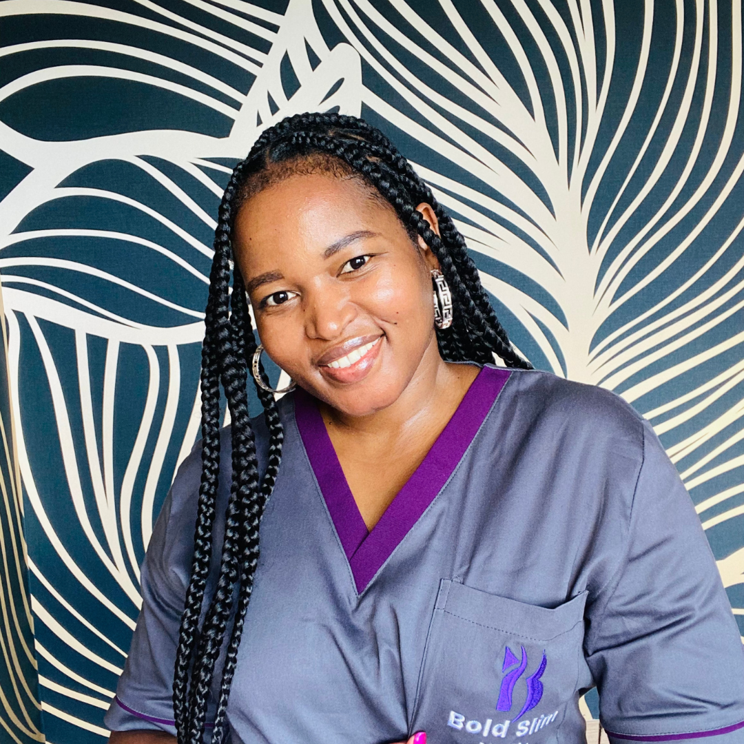 Smiling woman with braided hair in a gray uniform stands in front of a patterned wall.