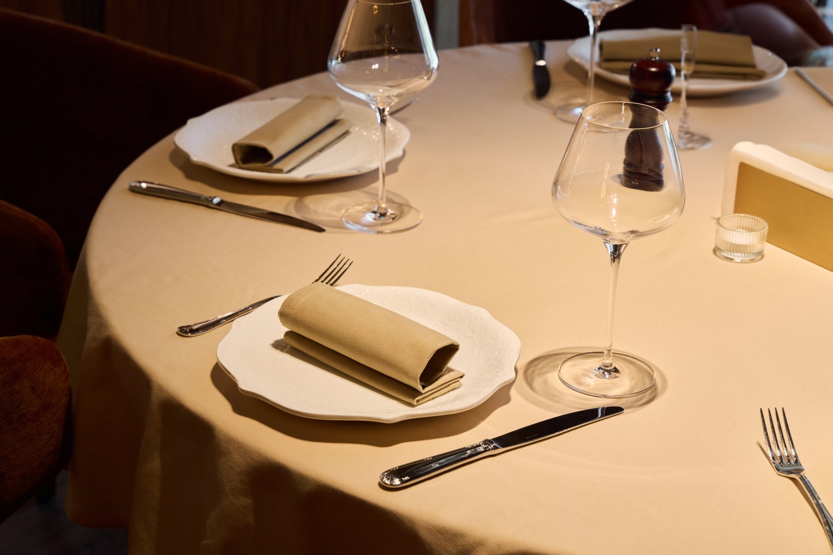 round table with white linens and glassware, elegant place setting arranged for romantic dinner; folded napkin