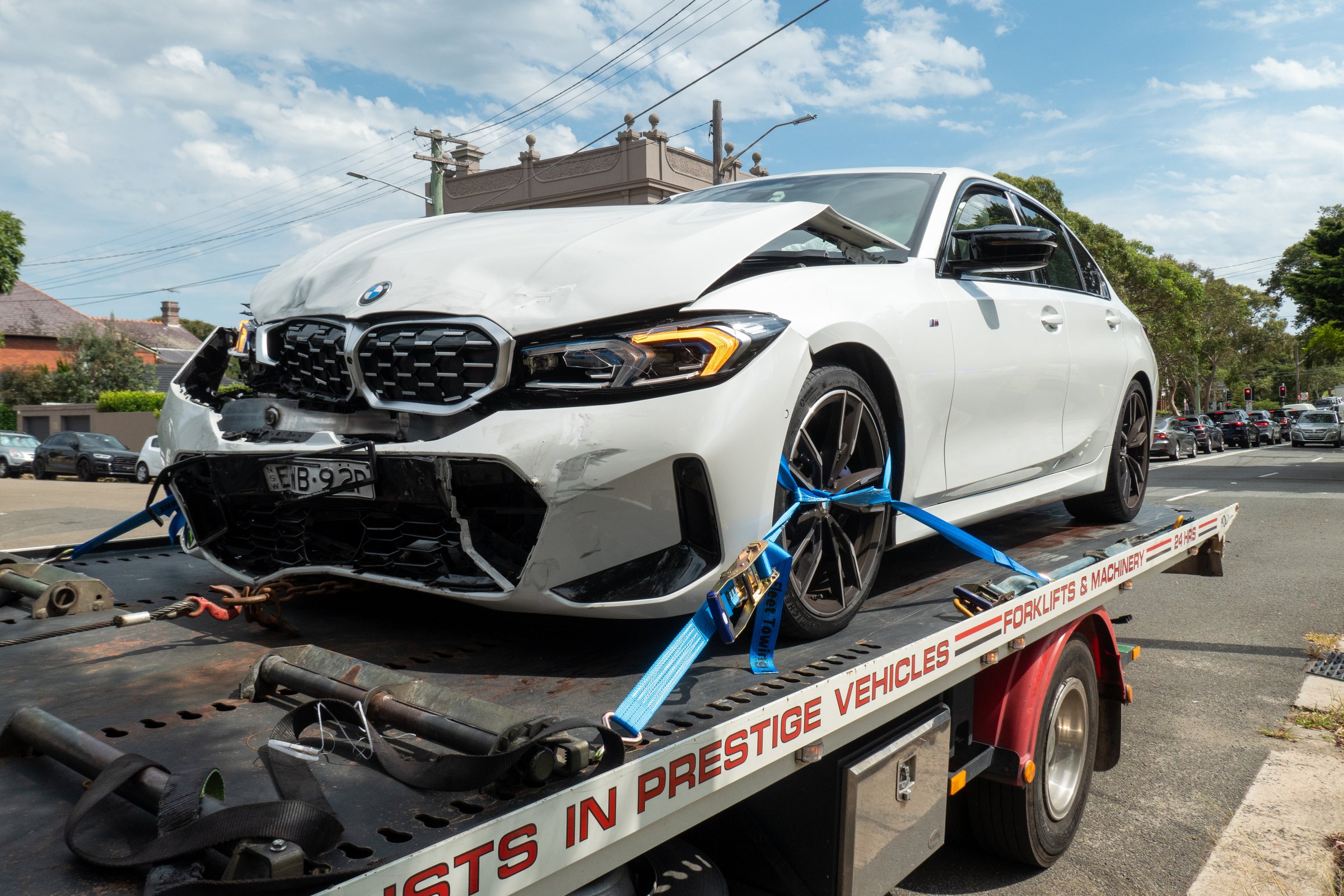 An electric BMW sedan on the back of a tow truck after being involved in a collision with another vehicle at the corner of Carrington Road and Pine Street, Randwick. The emergency indicator lights are still flashing. This image was taken on a hot and sunny morning on 8 February 2025.