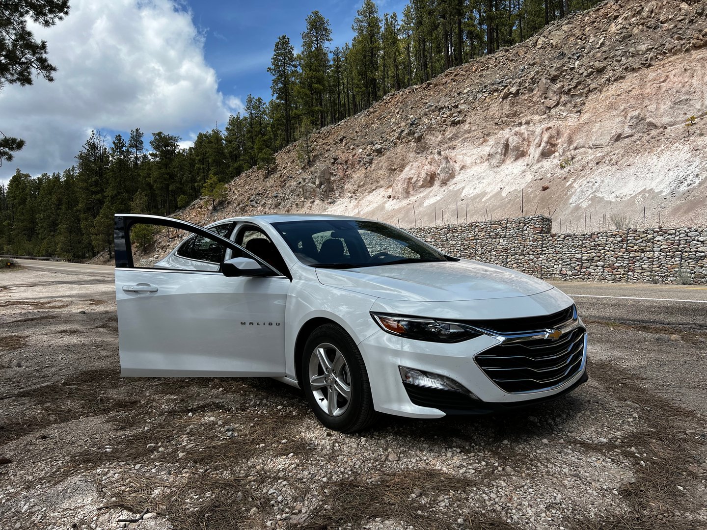 A white Chevrolet Malibu parked on a scenic road surrounded by pine trees in New Mexico. Ideal for travel content.