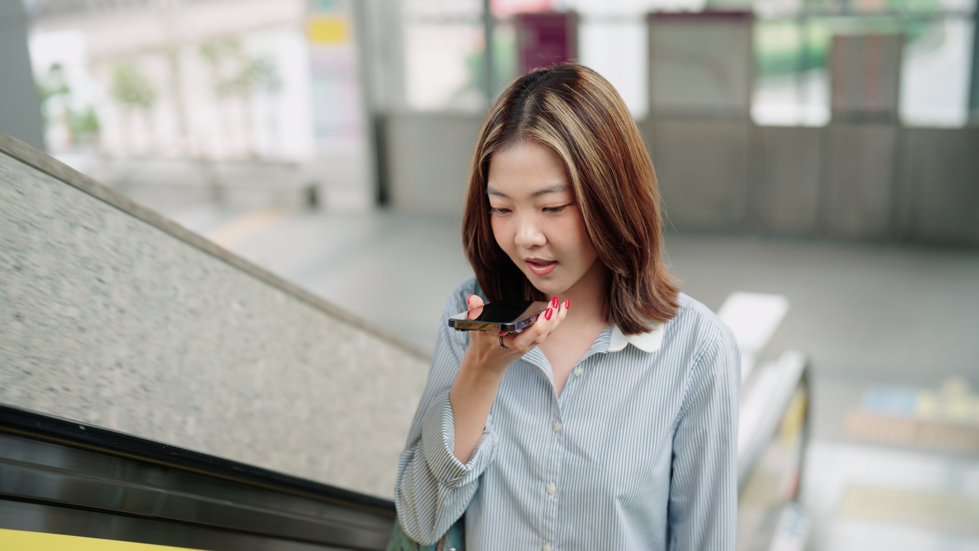 Female commuter interacting with an AI app on her phone while on the escalator.