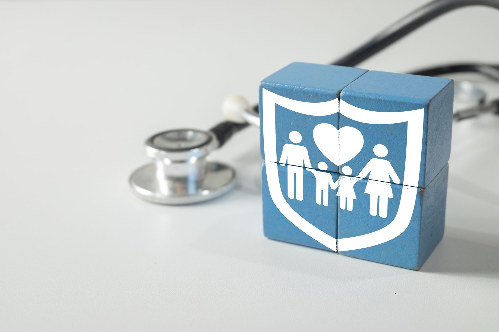 Family health insurance icon on wooden blocks with stethoscope on white background. Concept for medical protection, healthcare policy, family wellness, and affordable health coverage plan.