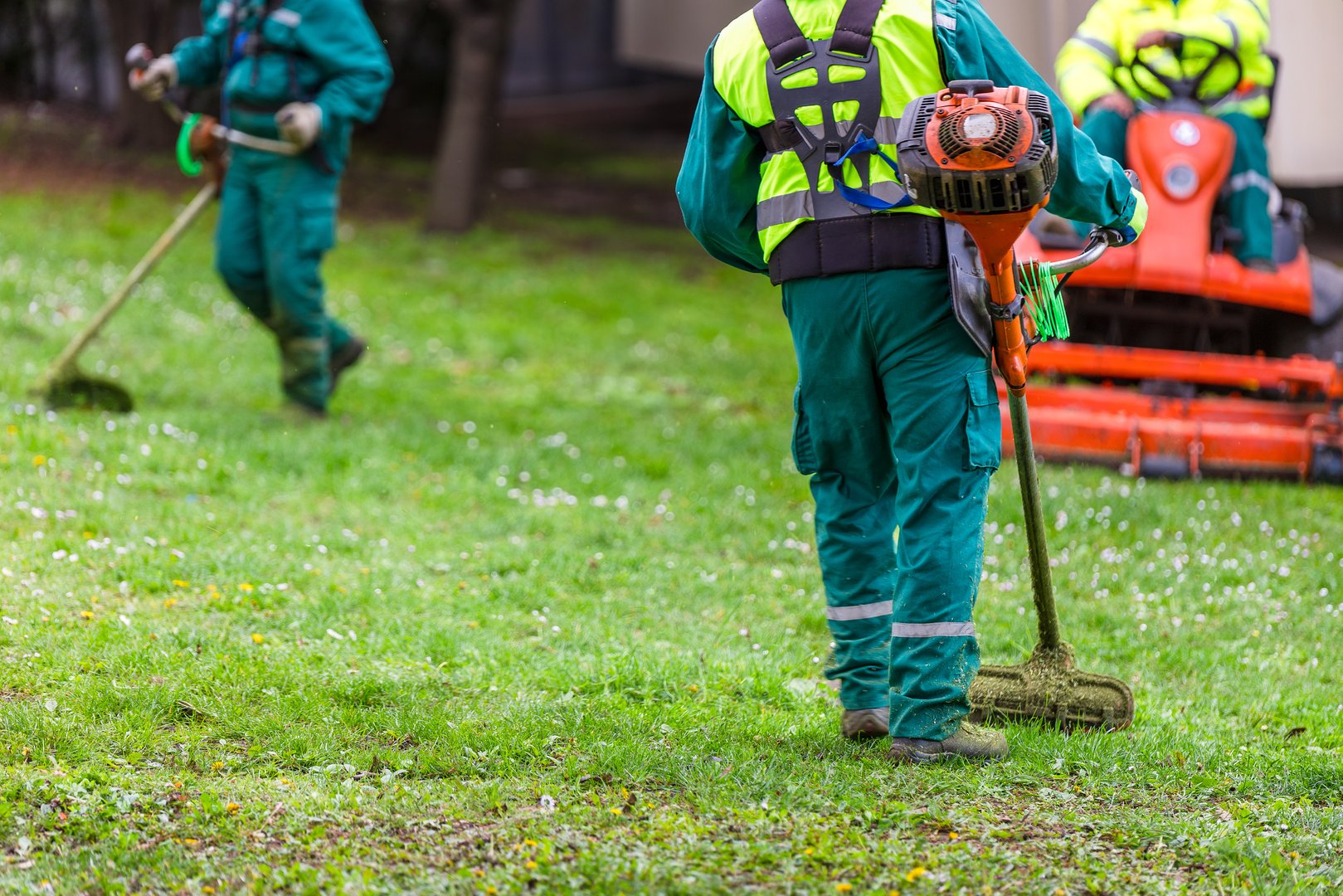 Three landscapers mowing and cleaning grass area