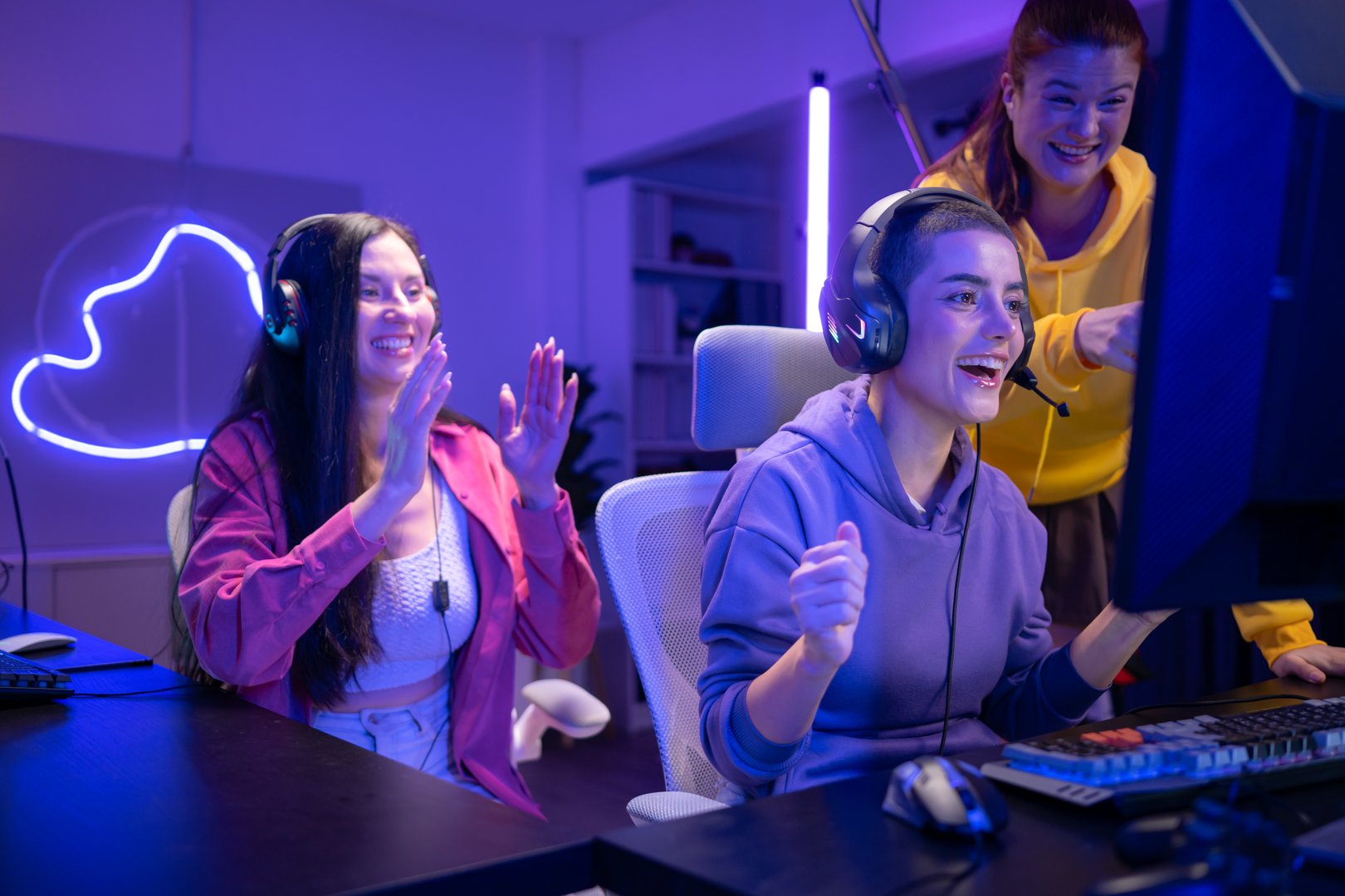 Group of woman play online game and celebrating a gaming victory in a neon-lit room, smiling and cheering while wearing headsets
