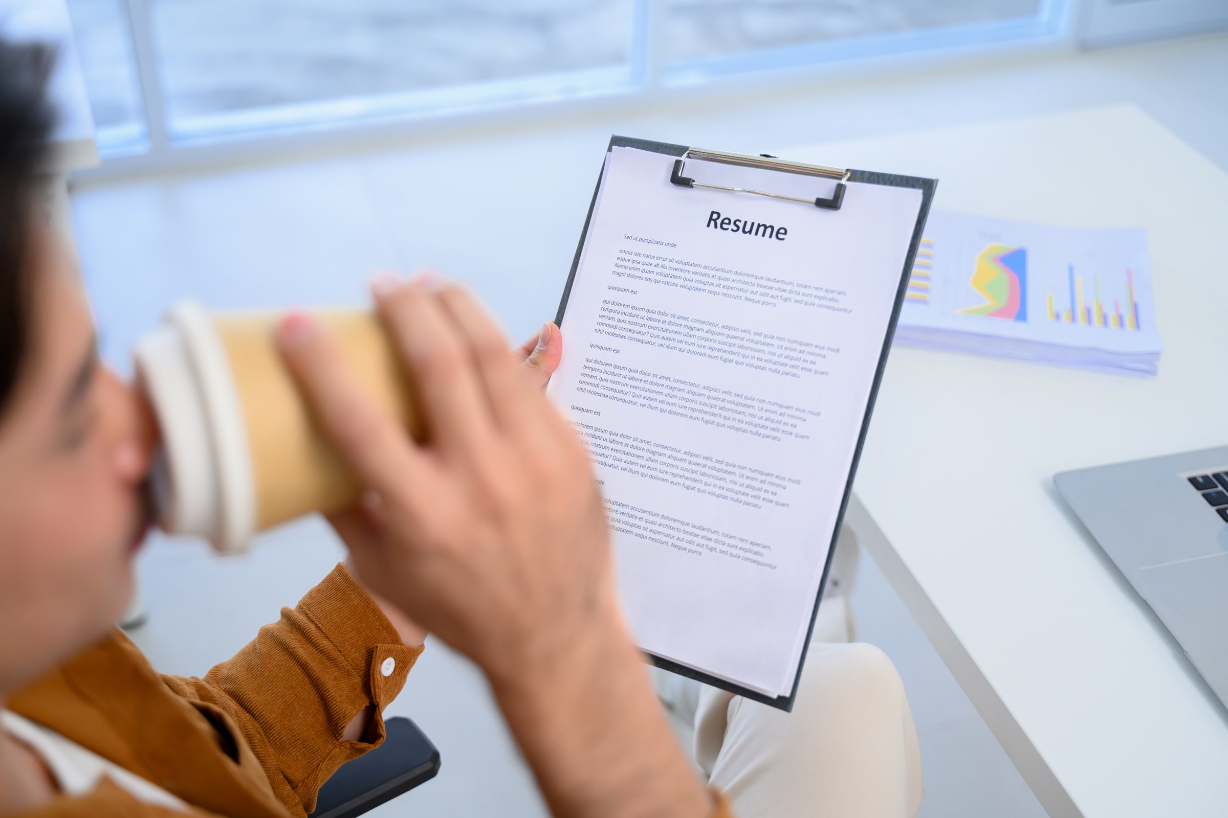 Cropped shot of HR manager sipping coffee reviewing resume during remote online job interview.