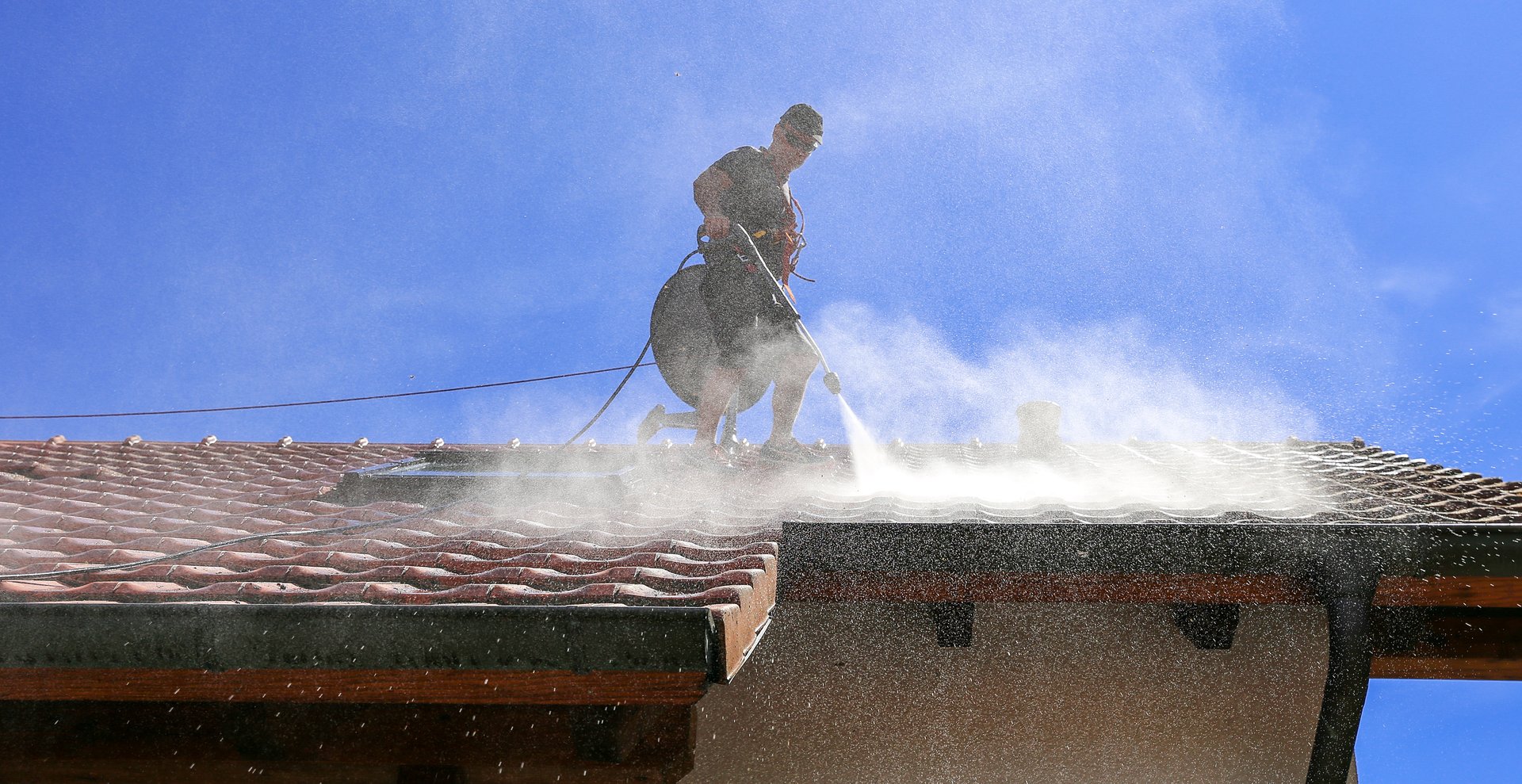 Workers cleaning the roof of moss and dirt with a high pressure cleaner