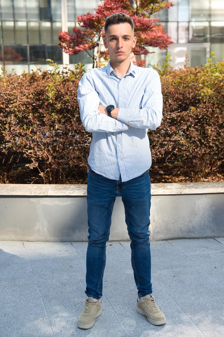 Man in a blue suit, white shirt, and patterned tie, standing against a white backdrop.