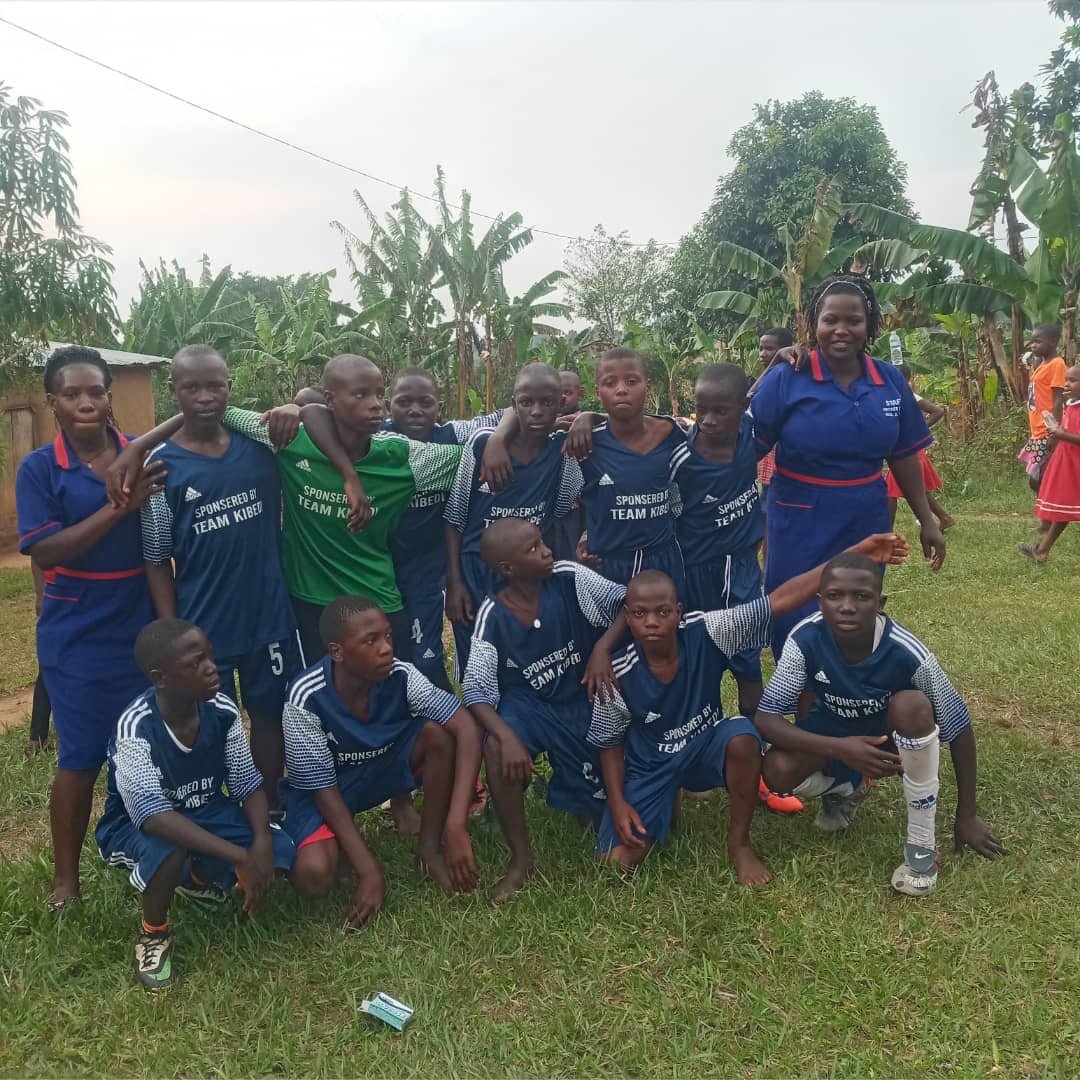 A youth soccer team poses for a group photo outdoors with their coach. Theyre wearing blue jerseys and standing on grass.