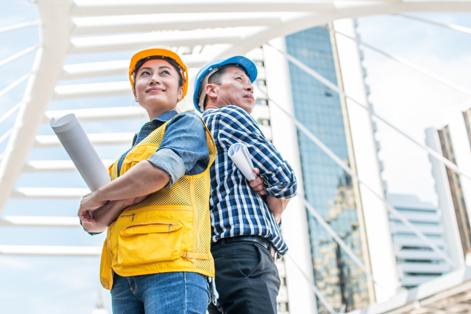 Industrial engineer wear safety helmet engineering standing with arms crossed holding inspection tablet and smile on building outside office. Engineering tools and construction concept.