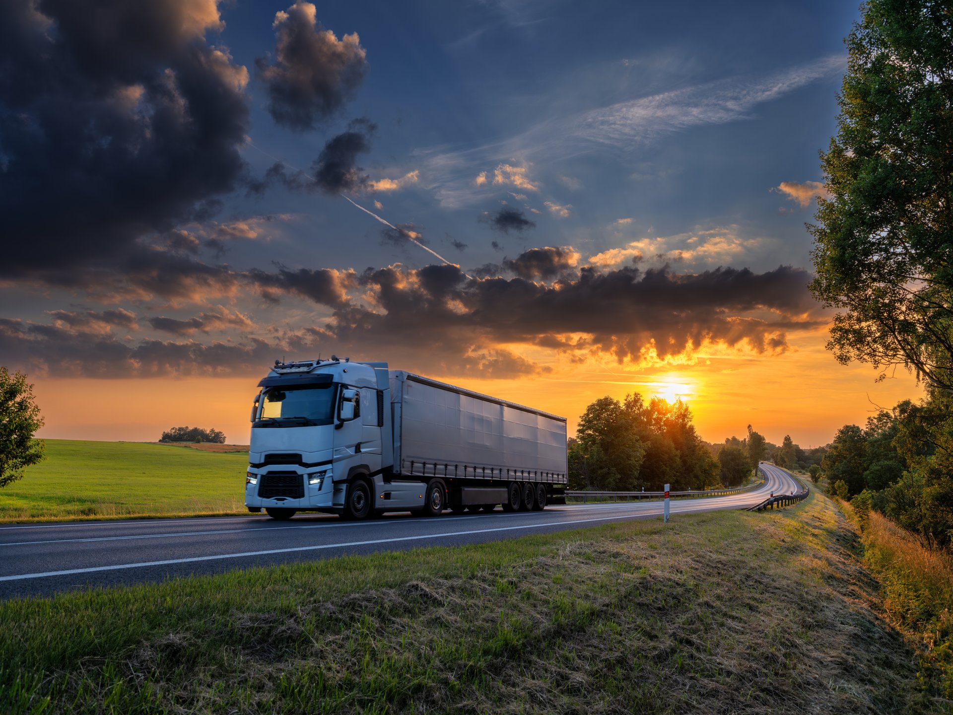 White truck driving on the asphalt road in rural landscape at sunset