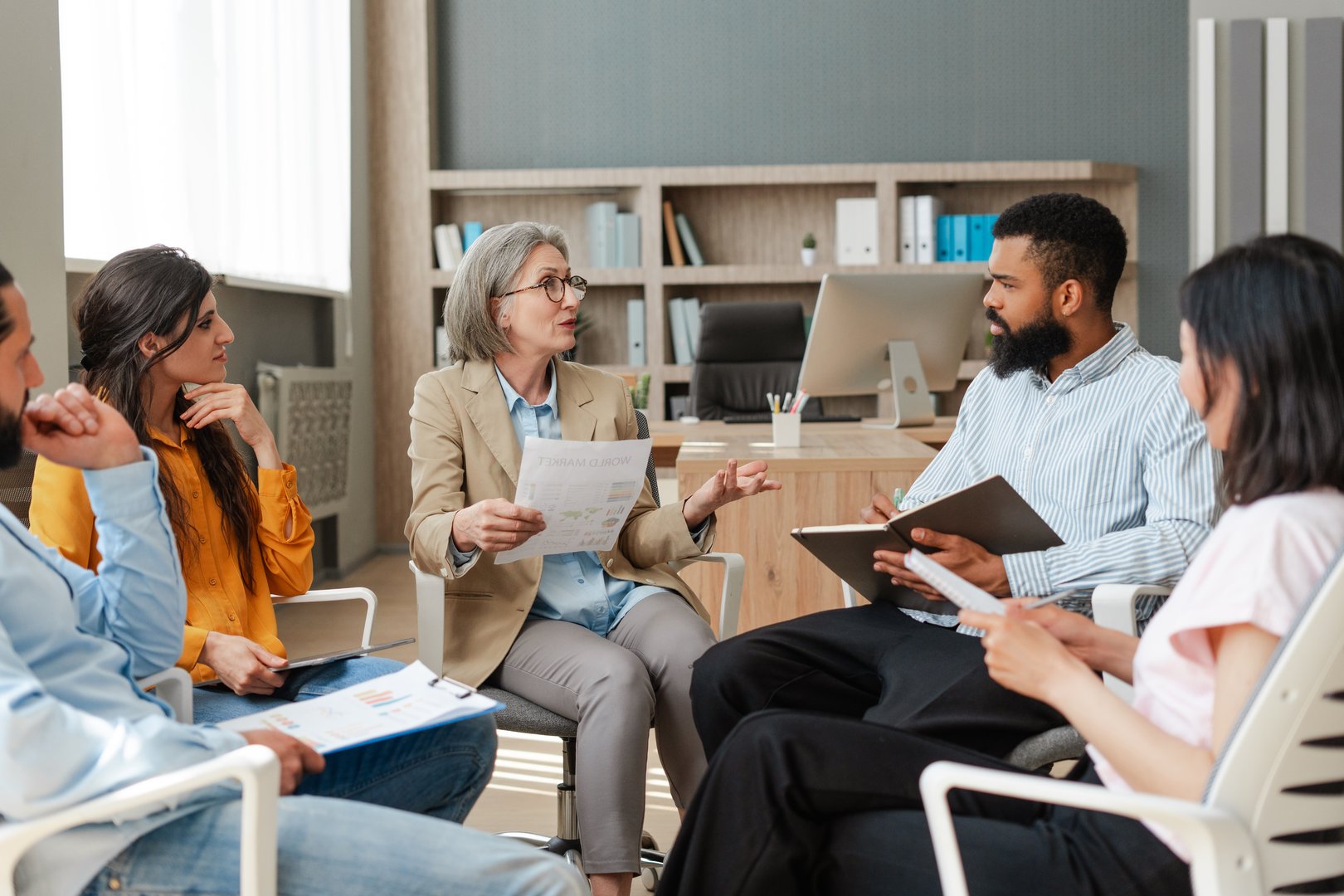 Diverse team of professionals is sitting in circle in modern office, listening to their leader presenting a project. Teamwork concept, presentation