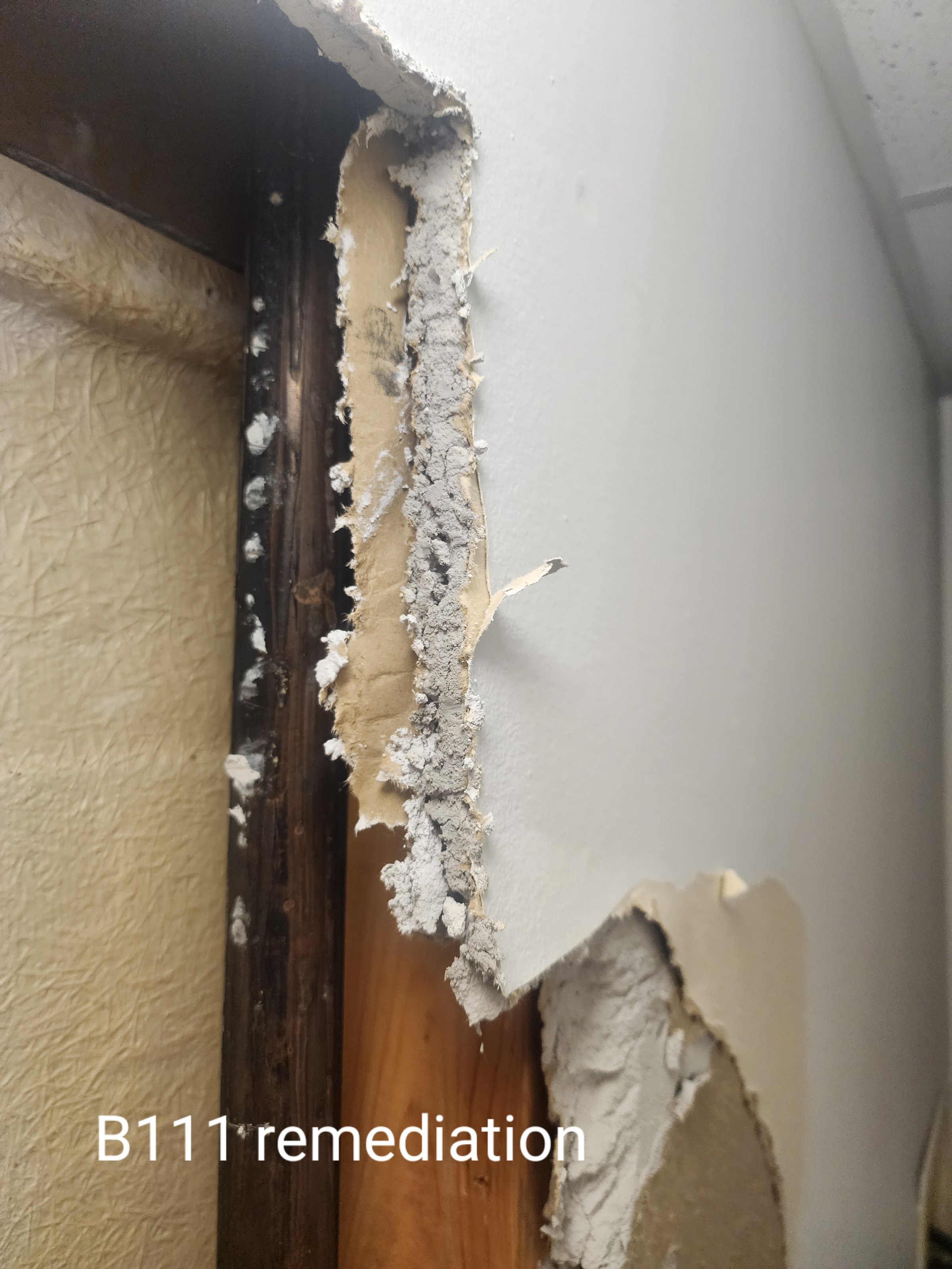 Damaged drywall showing exposed interior material near a doorway, labeled "B111 remediation."