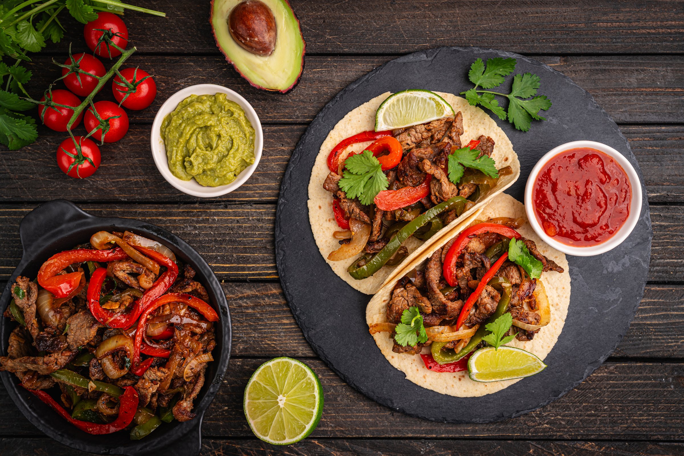 Fajitas, beef meat slices with colored pepper and onions, traditional mexican food, served with tortillas, salsa and sour cream on wooden background, top view. High quality photo