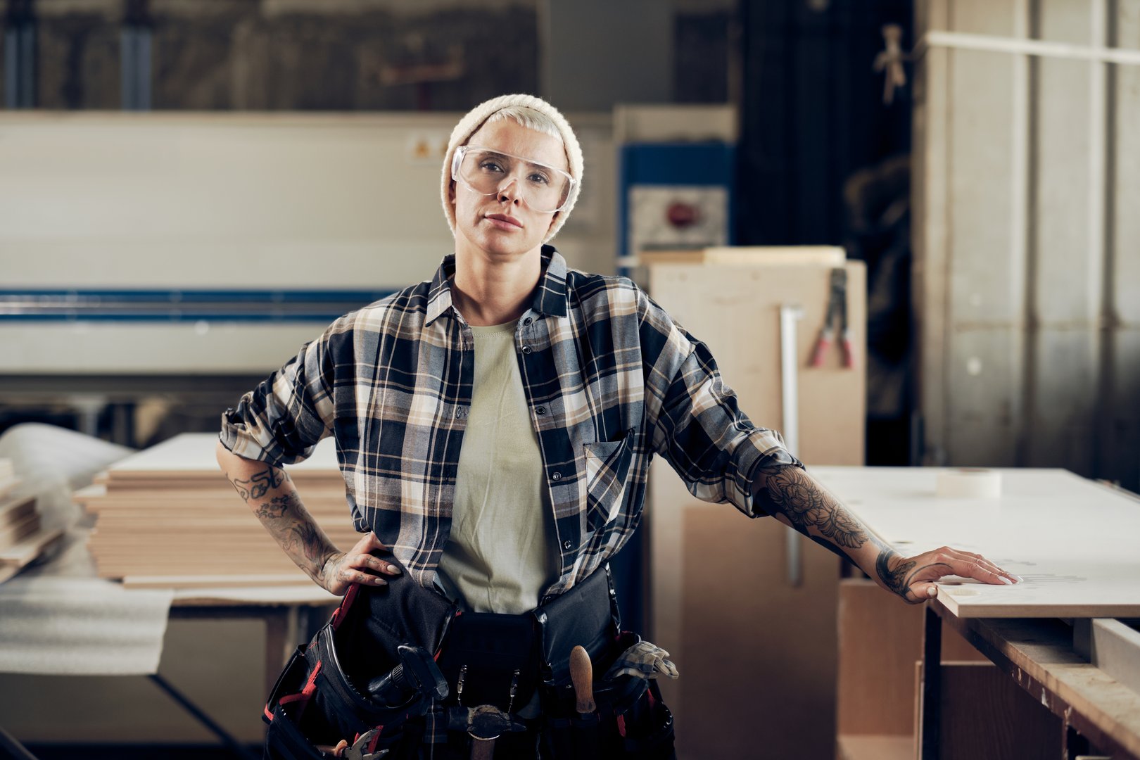 Portrait of tattooed woman in her 40s working at the wooden workshop, wearing protective gear. Concept of motivated women, gender equality, image of femininity in modern world