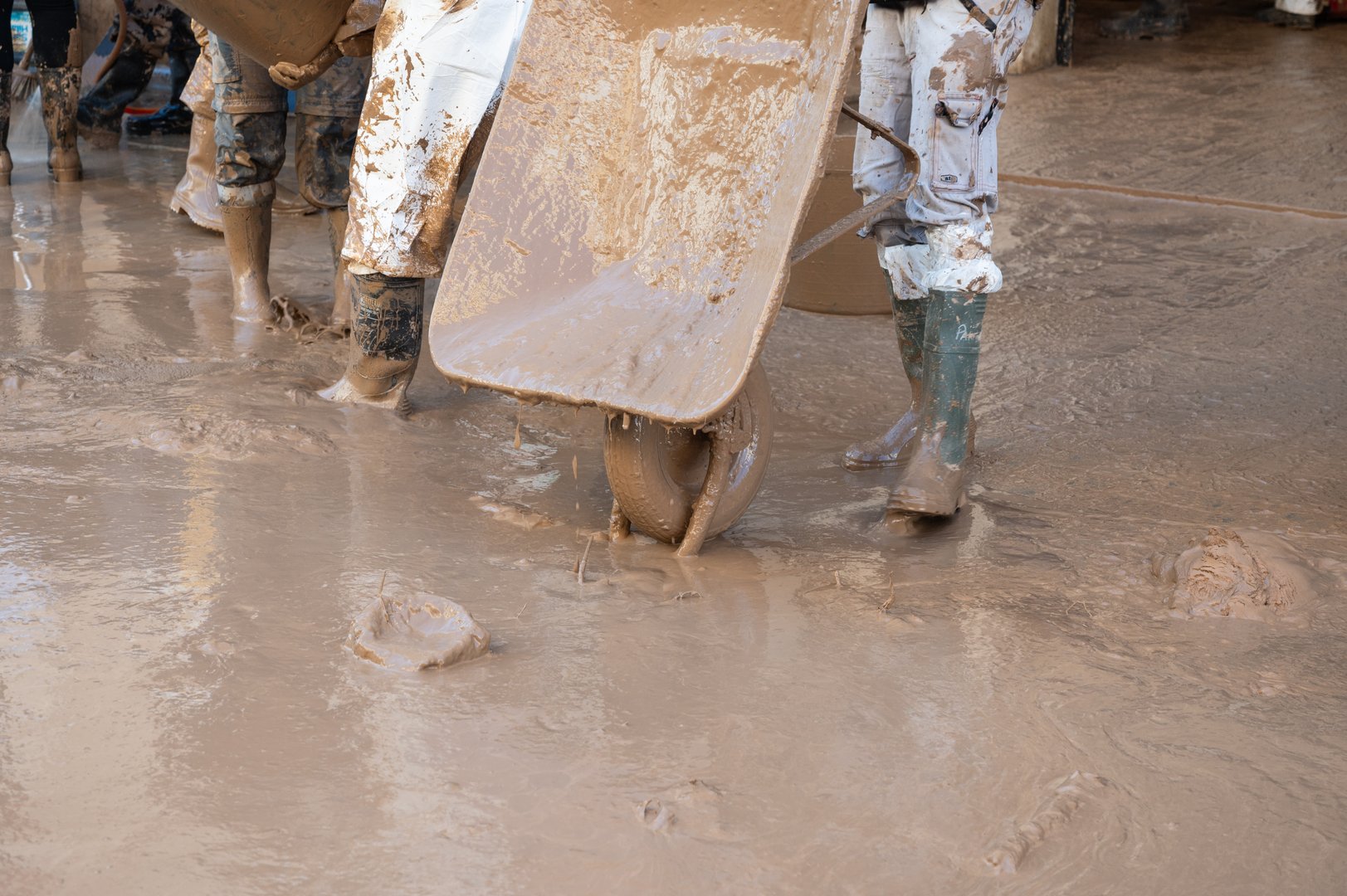 Volunteers with wheelbarrows cleaning a muddy street after a storm in Valencia, Spain