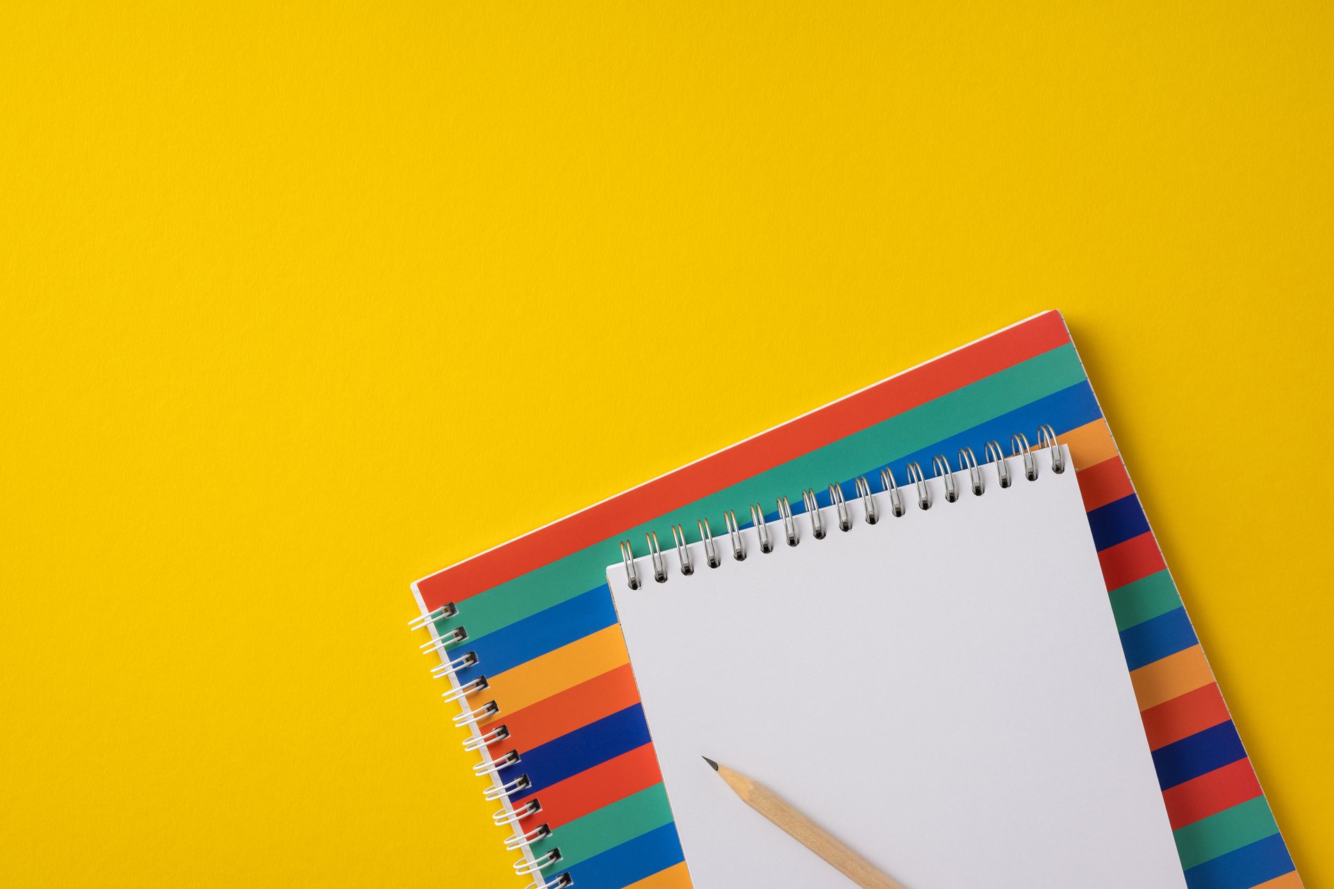 Notebook with a pencil placed on a vibrant, colorful striped surface against yellow.