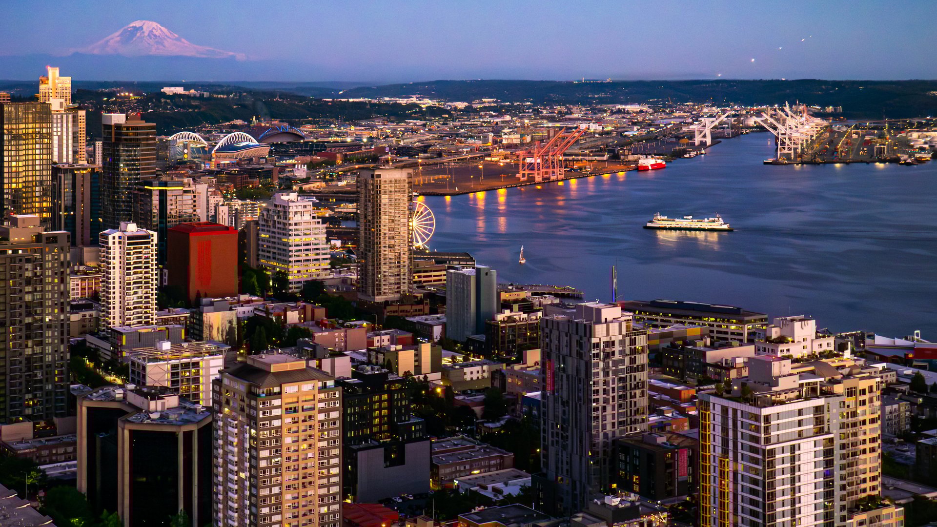 Aerial view of downtown Seattle, Washington, at dusk with Mount Rainier on the horizon, Puget Sound to the right, and a cruise ship coming in to port.