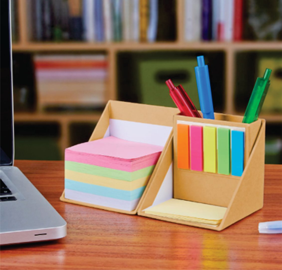 Desk organizer with colorful sticky notes, pens, and notepads on a wooden table next to a laptop in an office setting.