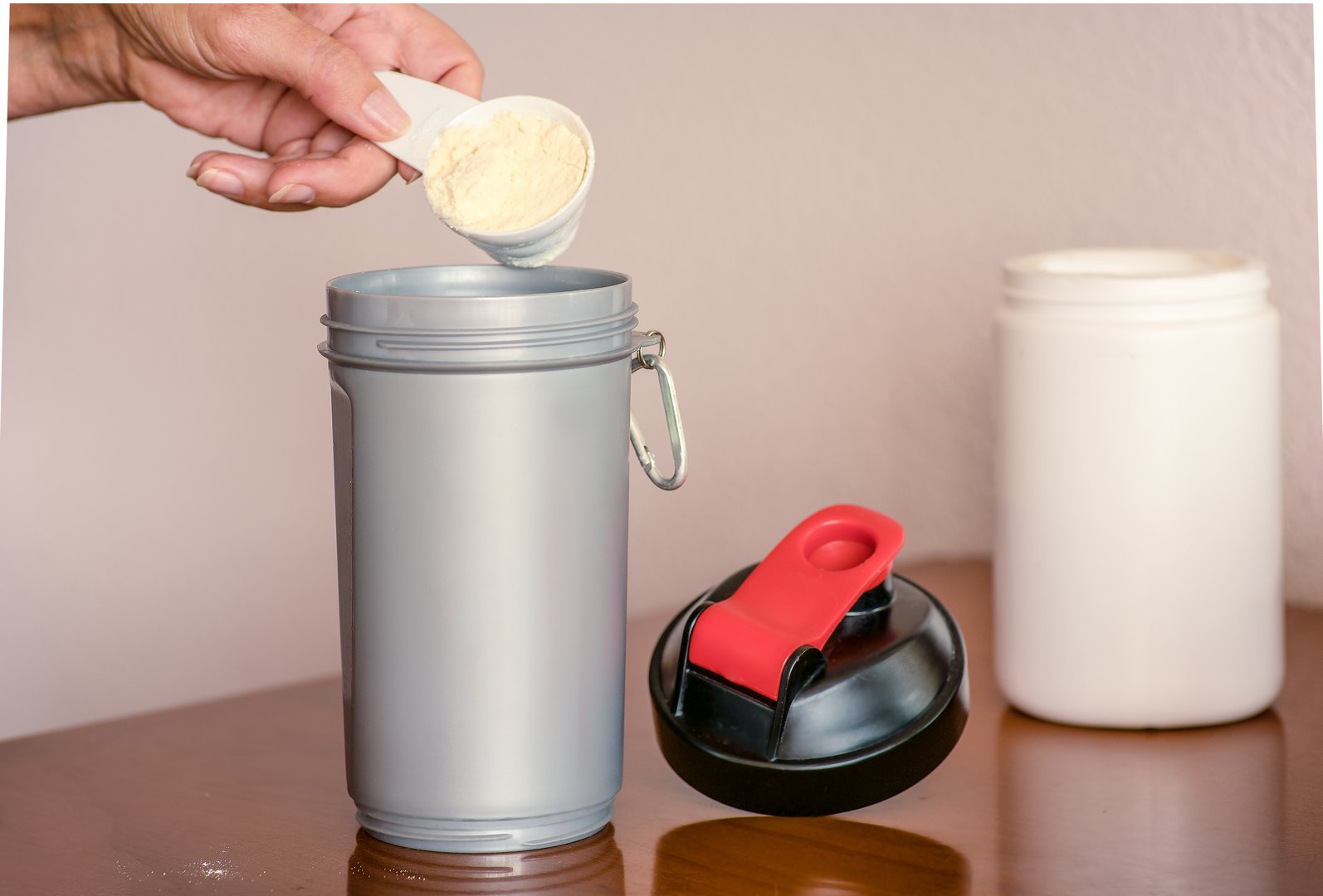 Woman's hand holding scoop while adding protein powder to protein shaker bottle. Body care and healthy lifestyle concept