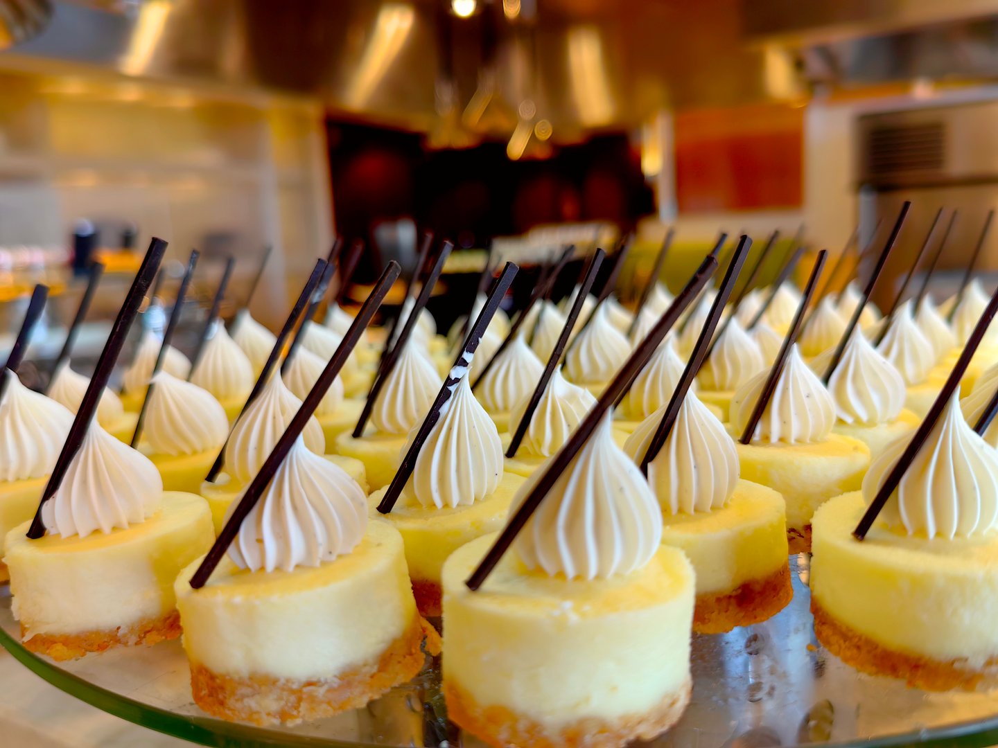 A row of delicious cheese cakes on the store tray, cakes with cream and chocolate sticks on top.