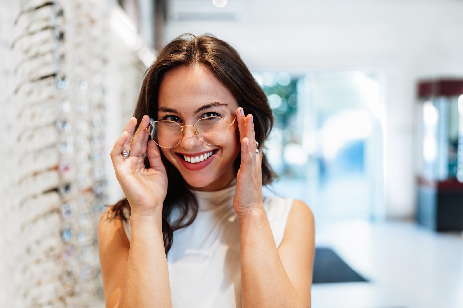 Cheerful young woman trying on eyeglasses in an optical store. She is smiling and looking at the camera, showcasing the latest eyewear trends and the importance of vision care