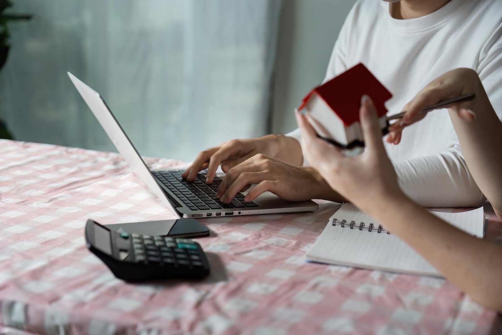 A couple strategizes their savings and investments for buying a new house, using a laptop and calculator at home.