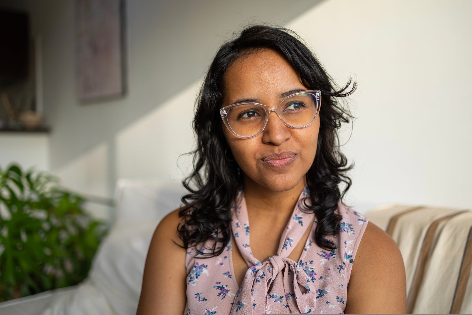 Portrait of young Hispanic woman with a glasses in the apartment with lot of sunlight looking away with a big smile