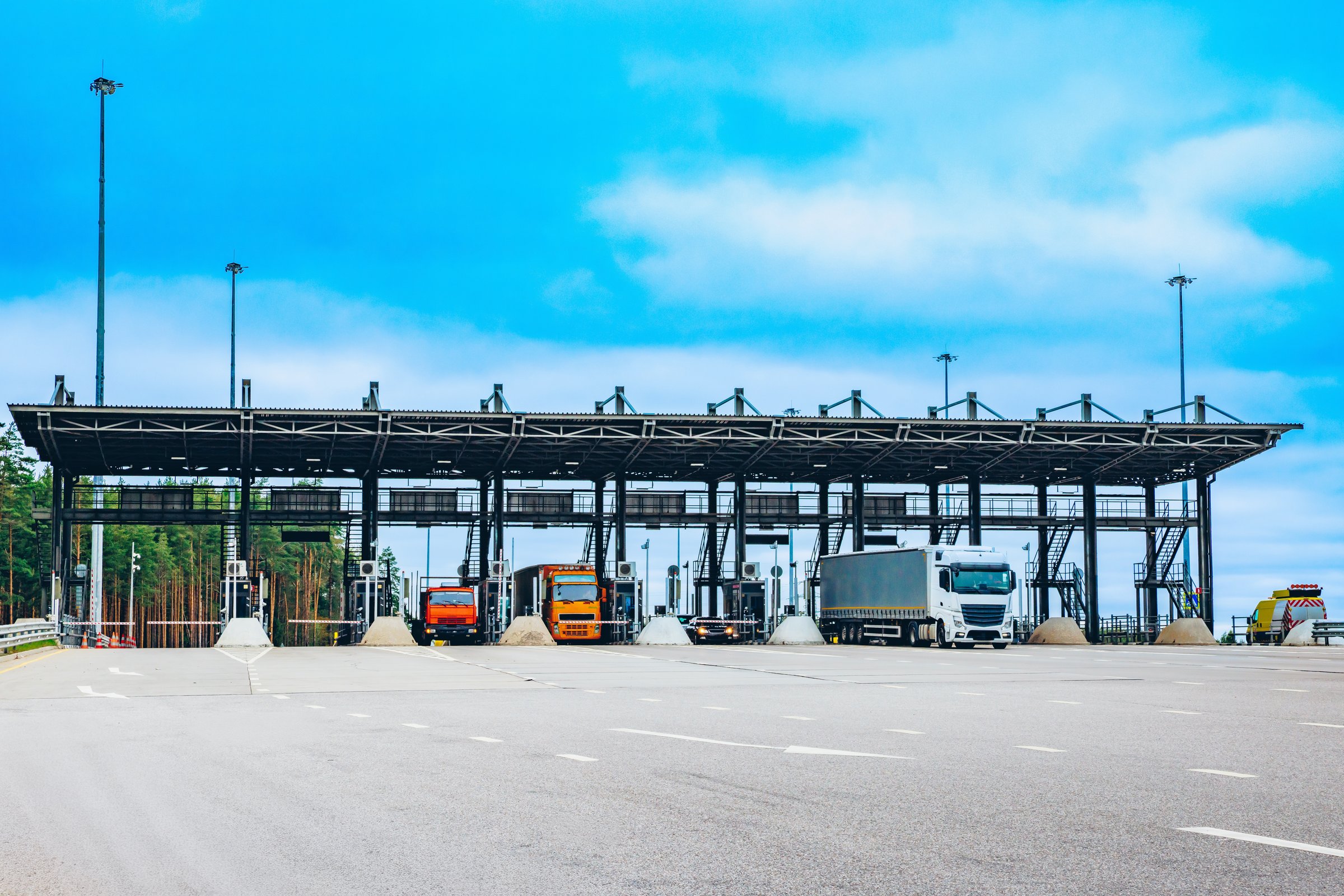 Trucks and Vehicles at a Toll Booth Station Under a Bright Blue Sky with Soft Clouds