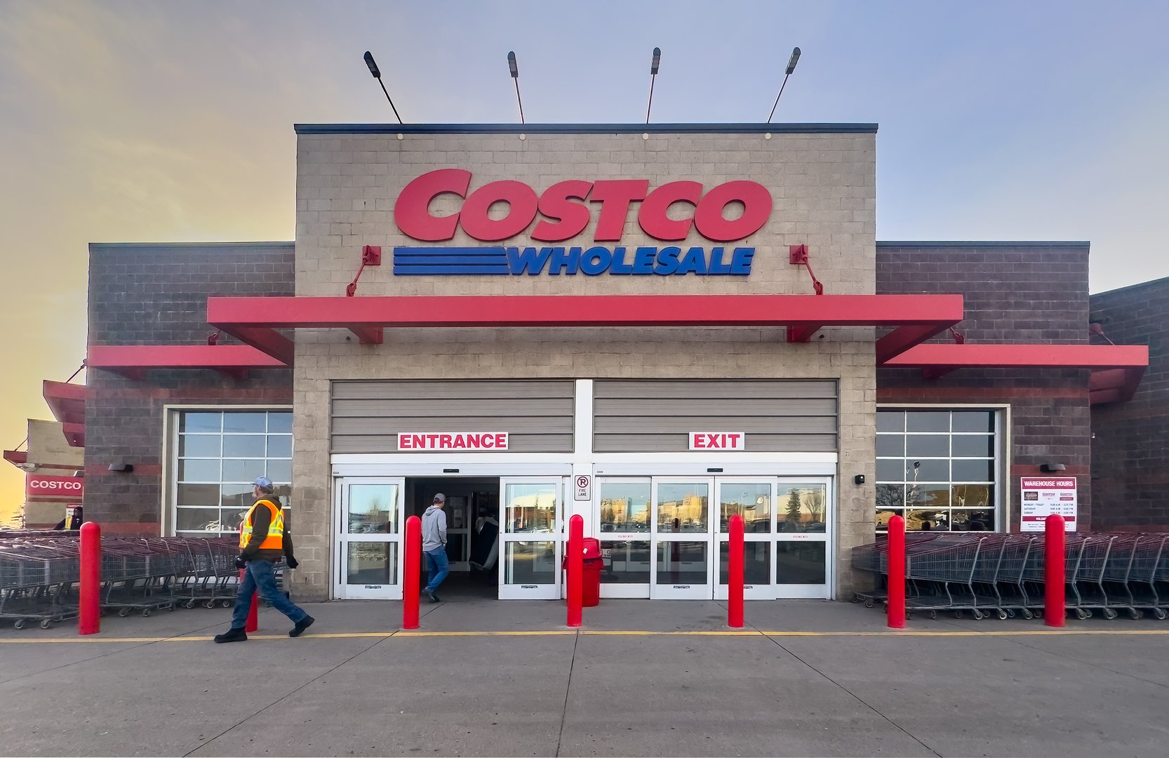 Calgary, Alberta, Canada. Apr 10, 2025. Exterior shot of a Costco Wholesale store at dusk with Costco Wholesale signage and people entering, exiting. Shopping carts visible