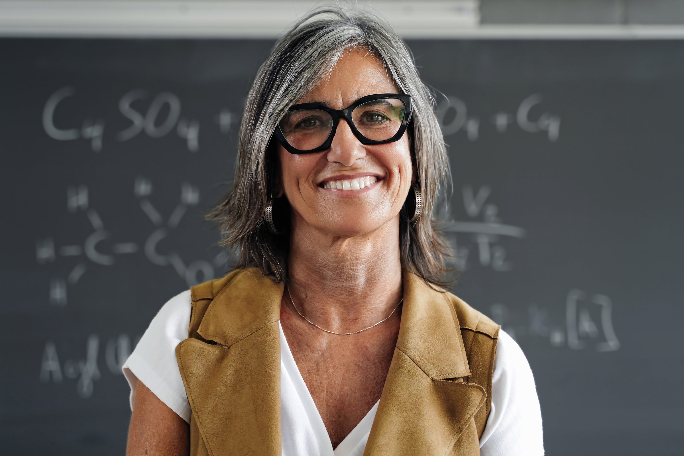Mature female professor standing college classroom smiling looking at camera. Happy High School woman science teacher