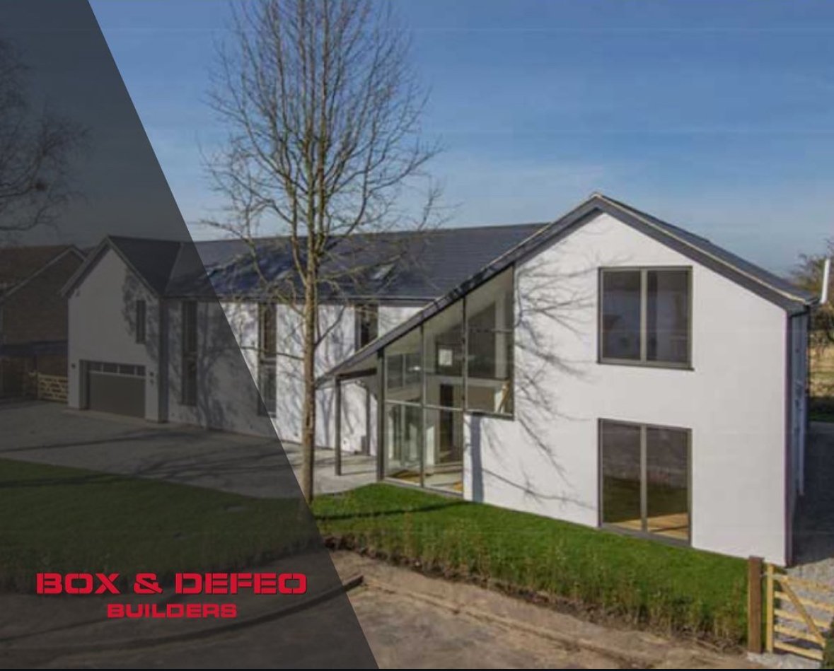 Modern luxury home exterior with large windows, stone facade, and spacious driveway at sunset.