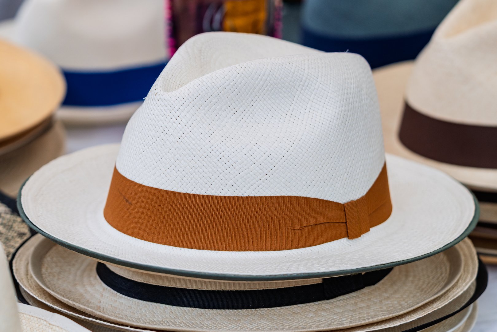 Stylish Panama hat with brown band shown on top of stacked hats at a local market. Great for fashion, summer, and cultural themes.