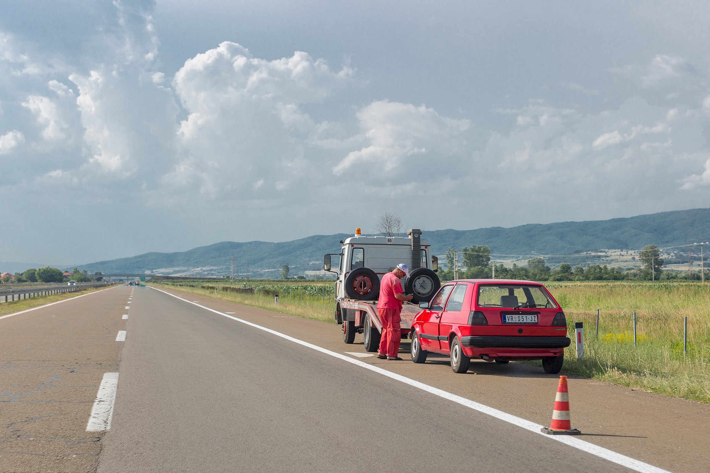 Vranje, Serbia – June 23, 2019: Towing service worker is going to load old damaged car on tow truck on highway. Old red Volkswagen Golf