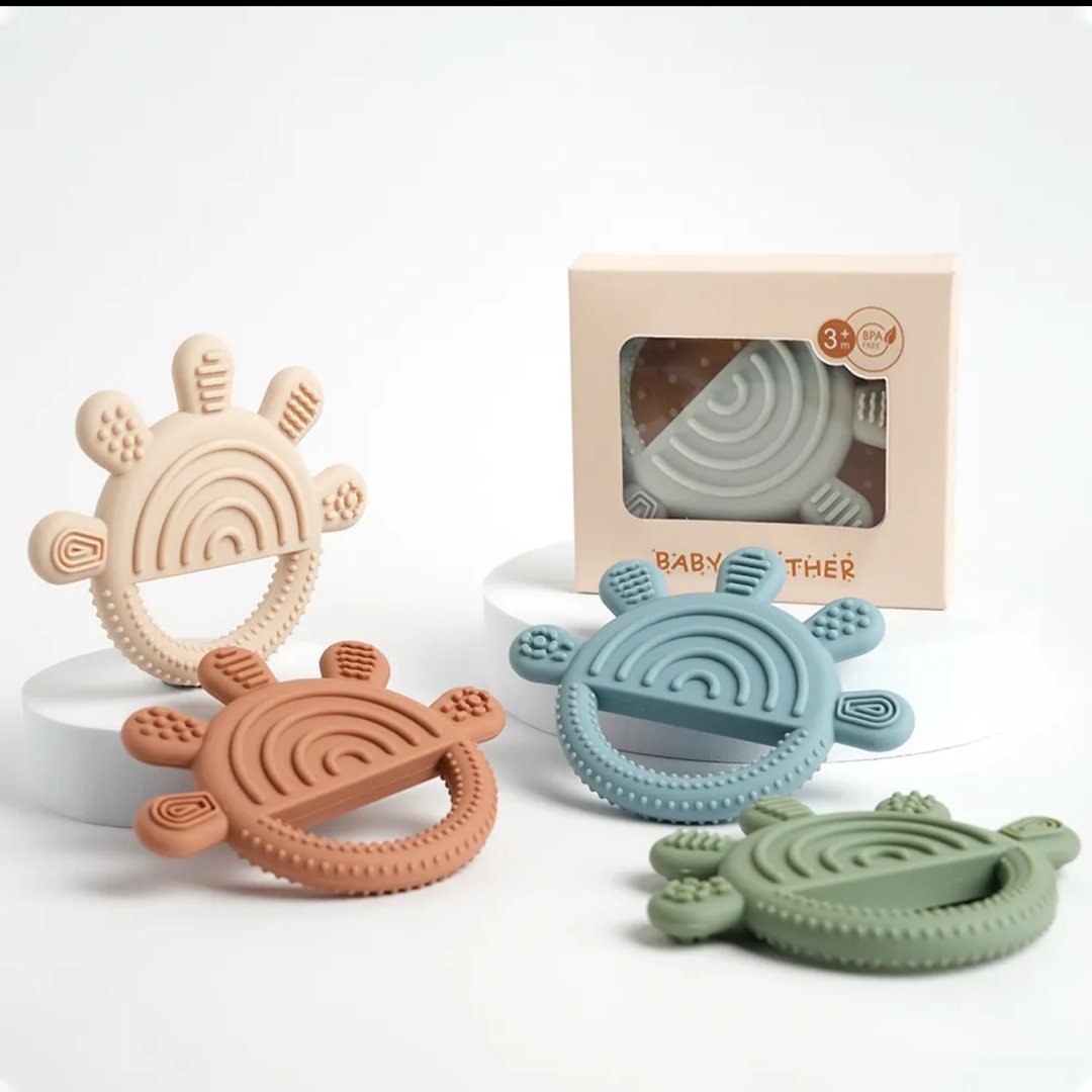 Colorful silicone baby teething rings in rainbow shapes with packaging, displayed on a white surface.