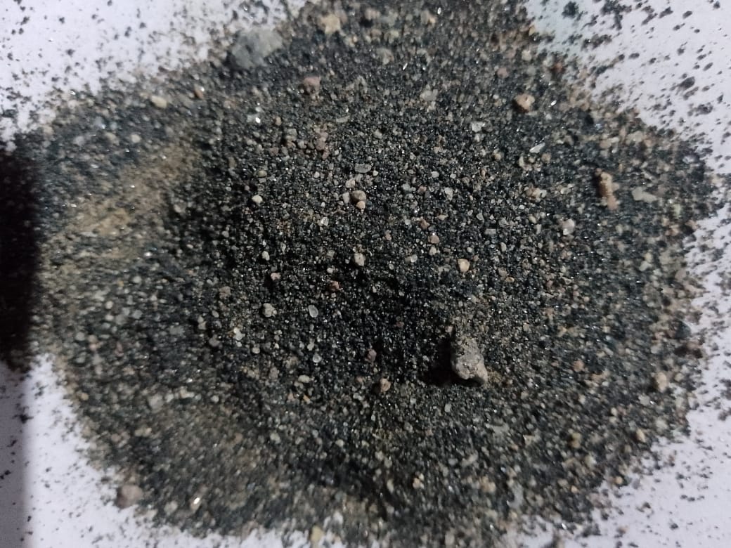 Close-up image of dark, coarse-grained sand with small pebbles on a white background.