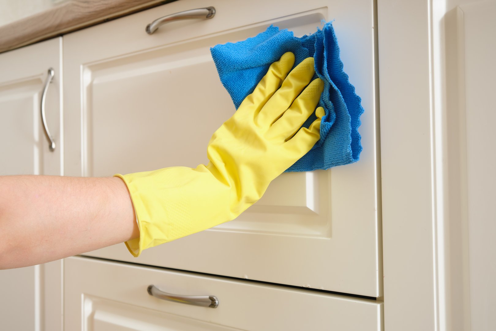 A woman washes furniture in her home kitchen with a blue cloth. Female hands in yellow gloves while cleaning the kitchen