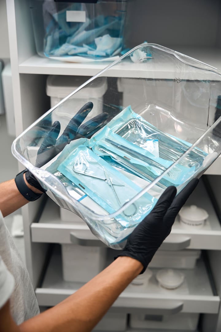 Lot of different medical tools in heat-sealing packages lying in transparent container, medical technician checking medical tools in storage