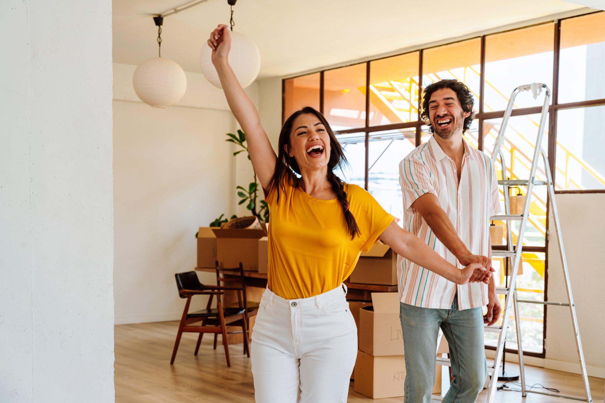 Happy young couple relocating in a new apartment. Young woman and man celebrating and dancing for the new property they just bought. Moving stuff and boxes together. Lifestyle concept about starting a new life and real estate business.