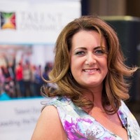 Woman with brown hair smiling, standing in front of a banner at an event.