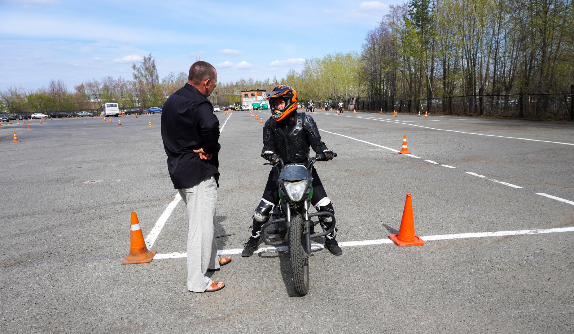 A young woman is learning to ride a motorbike in a motorcycle school. She is taught by a teacher.