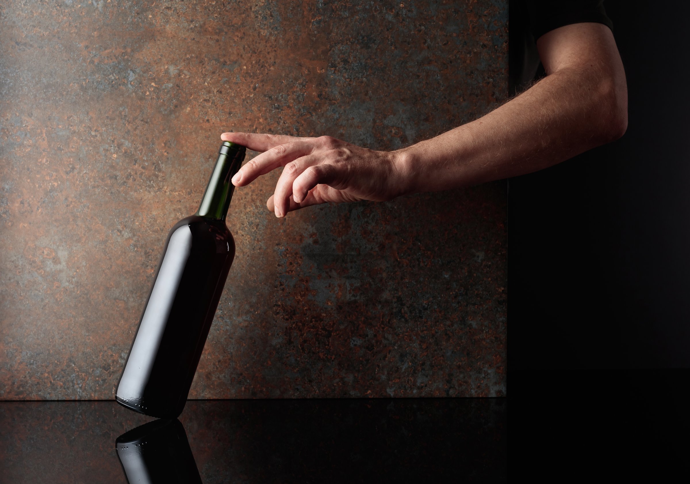 Hand reaches for a bottle of red wine. A concept image on the theme of expensive wines. Copy space.