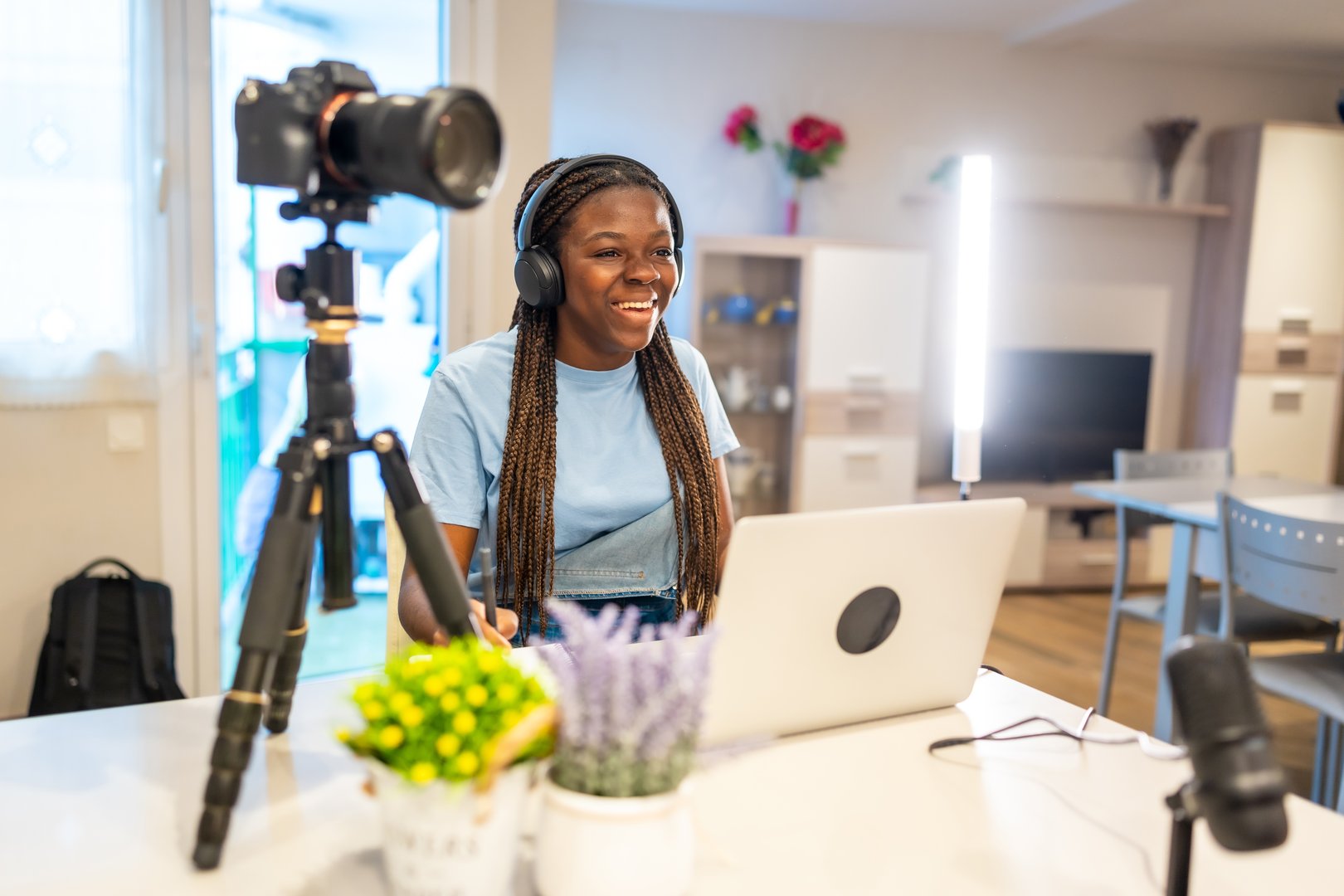 Smiling teenager creating video content for her vlog using a laptop, camera, microphone, and lighting equipment