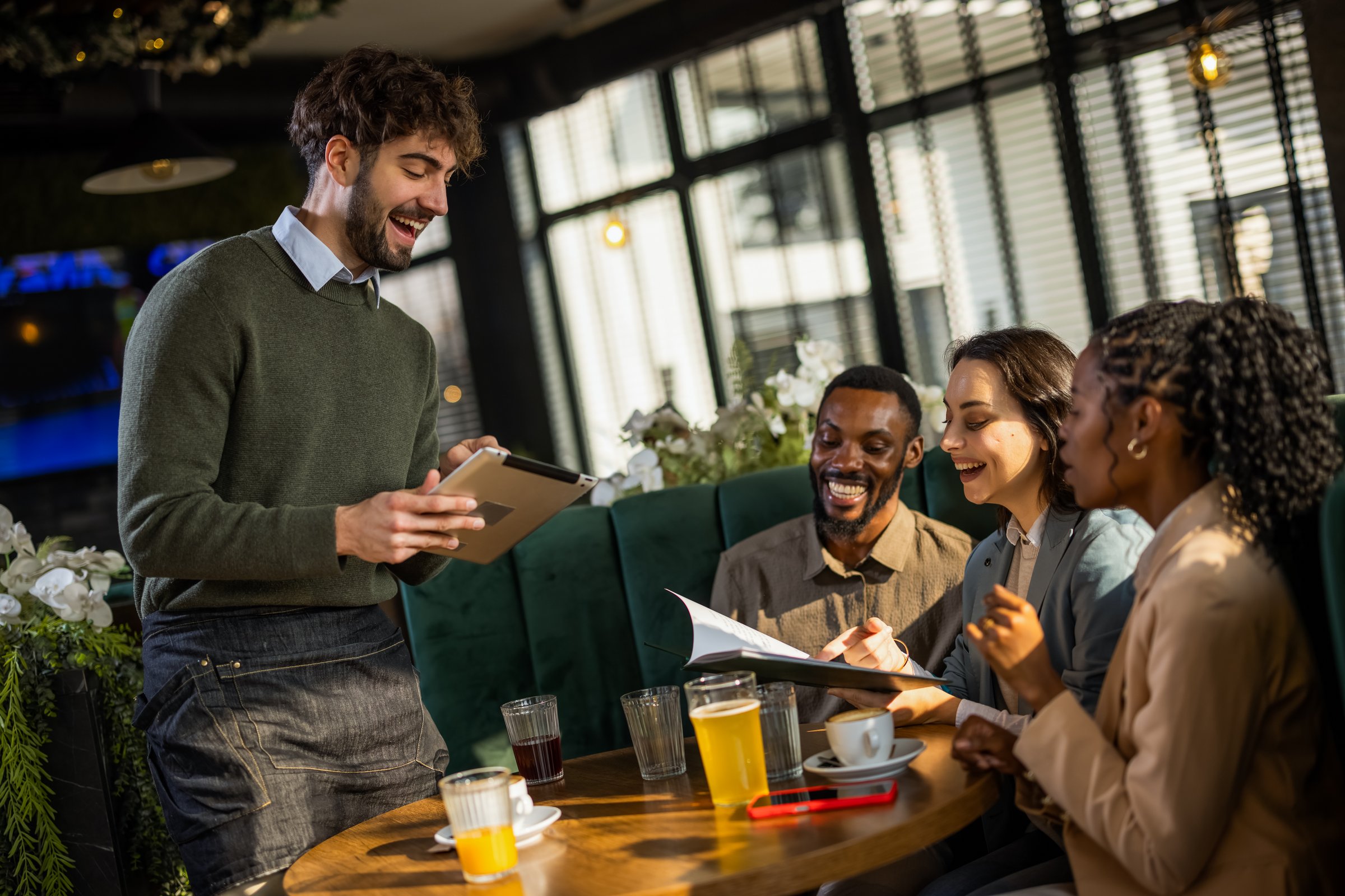 Waiter recording a group's order on a digital tablet in a cafe