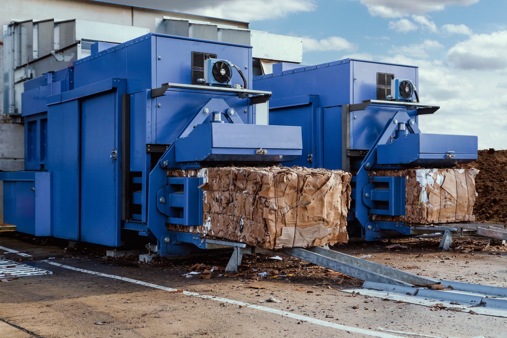 A blue paper squeezer container and a garbage press machine recycle cardboard into reusable material bales