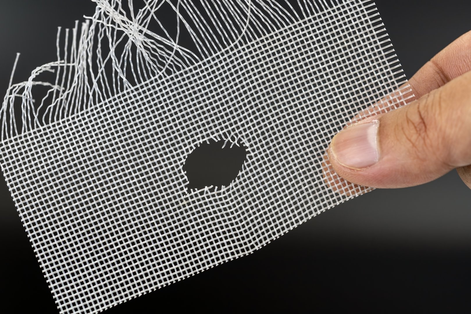A hand holds damaged wire mesh with hole, possibly caused by rat. mesh is frayed and shows signs of wear, highlighting need for repair or replacement